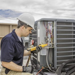 Trained hvac technician holding a voltage meter, performing preventative maintenance on a air conditioning condenser unit.